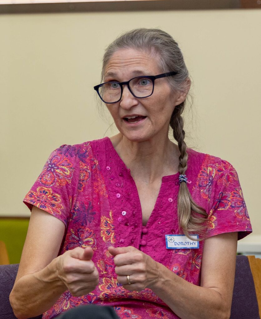 Dorothy Swain speaking, wearing glasses, a long braid and a pink floral shirt